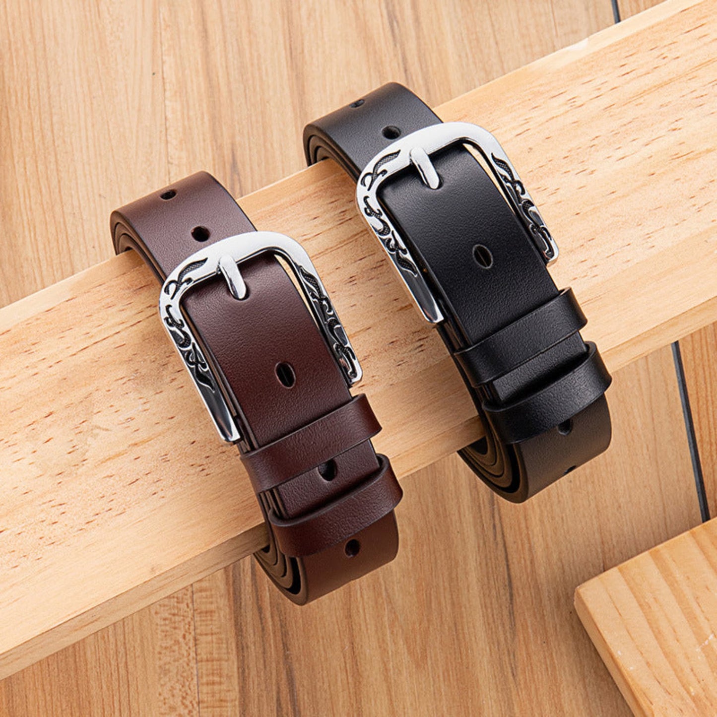 Women's Slim Black and Brown Leather Belts with Engraved Floral Silver D-Buckle Draped on Wooden Plank – Avenue