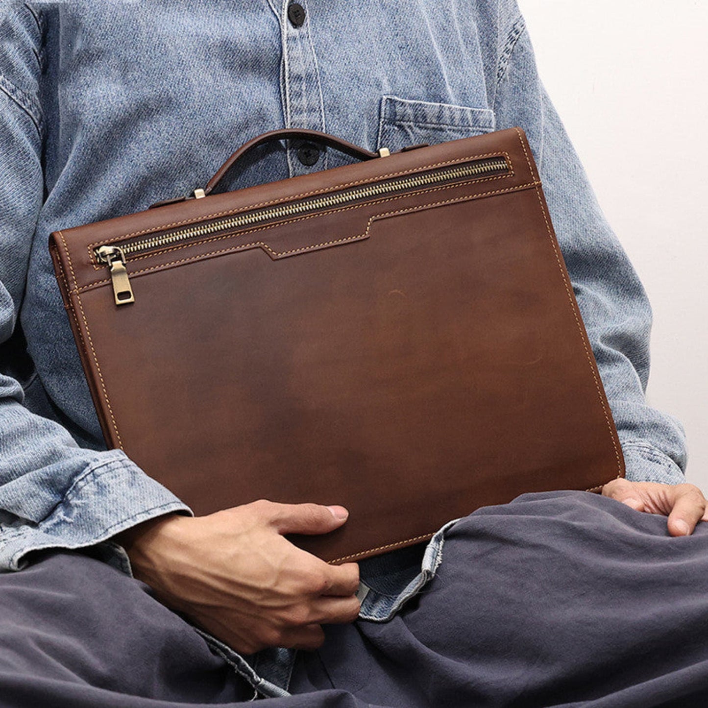Avenue Men's Crazy Horse Leather Laptop Briefcase 13.3 Inch — Man Seated Holding Briefcase on Lap Showing Back Zipper Pocket, Top Handle and Gold Hardware in Coffee Brown