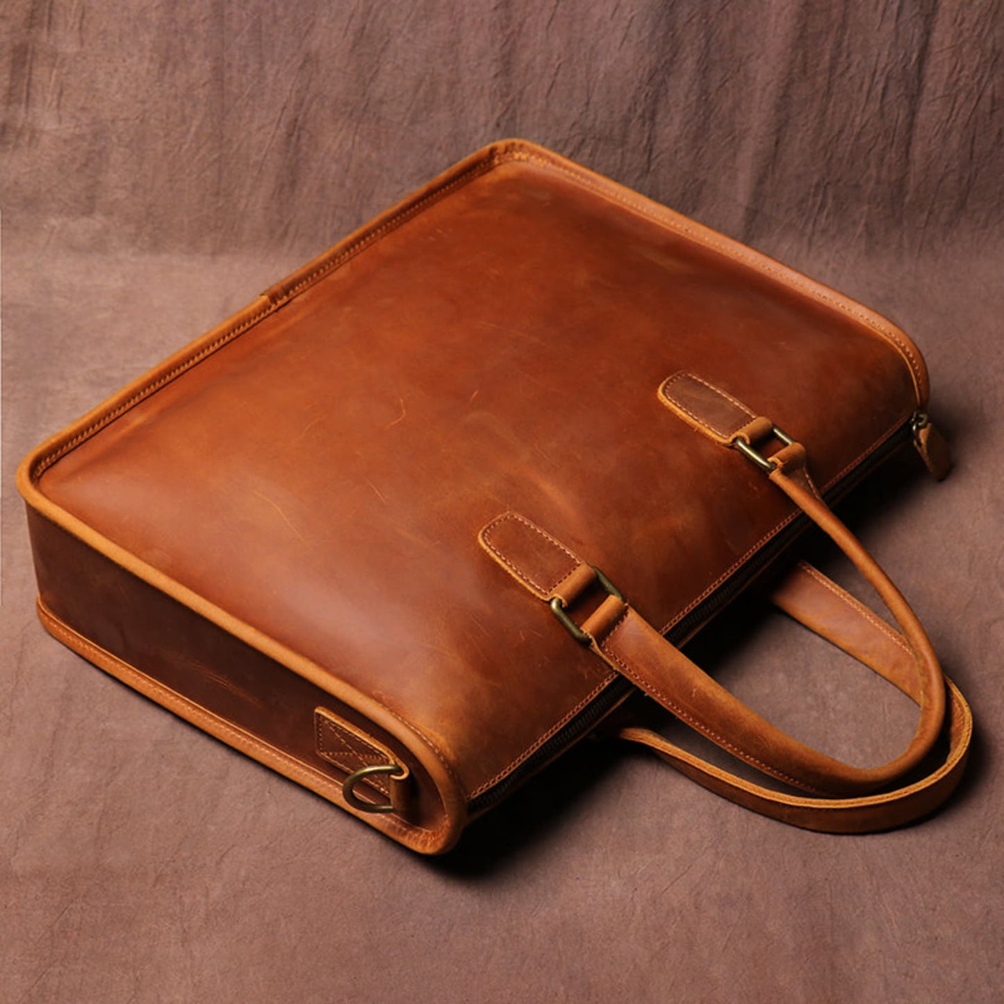 Men's Crazy Horse Leather Briefcase | Vintage Laptop Bag – Vintage Brown Top & Side Angle View Showing Zipper, Stitching, Top Handles, Antique Brass Hooks and Shoulder Strap Hook Detail on Brown Textured Background by Avenue