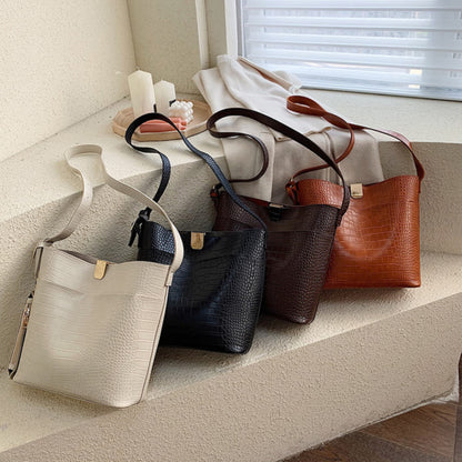 Women's one shoulder bucket bag in four colors — white, black, coffee and brown — croc-embossed PU leather with magnetic snap closure, arranged on a stone staircase | Avenue