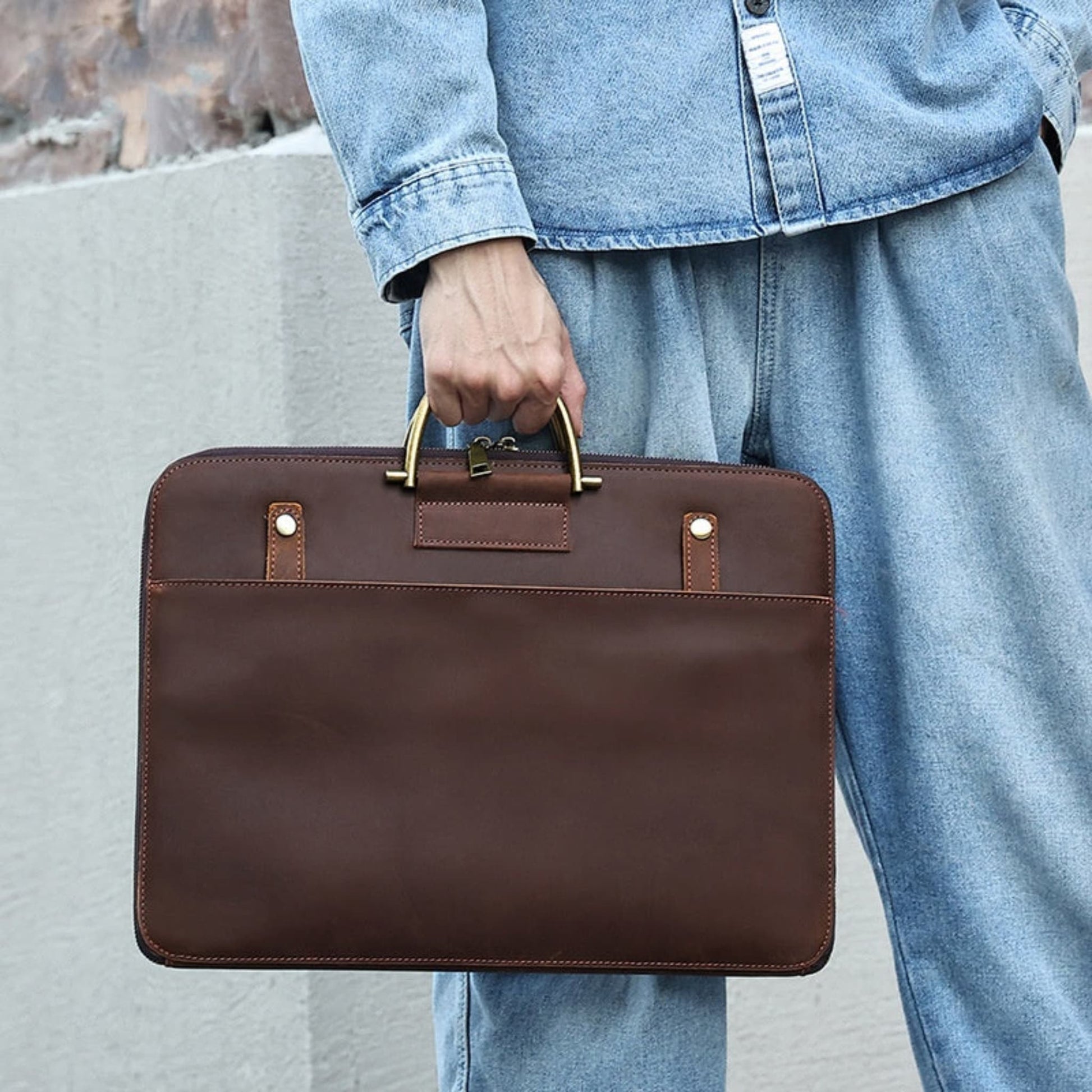 Avenue Crazy Horse Genuine Leather Briefcase for Men – Lifestyle shot in 2121 Brown, held by a man in denim outfit, showcasing antique brass top handle grip, brass stud detailing, front slip pocket, and contrast stitching against an outdoor stone background