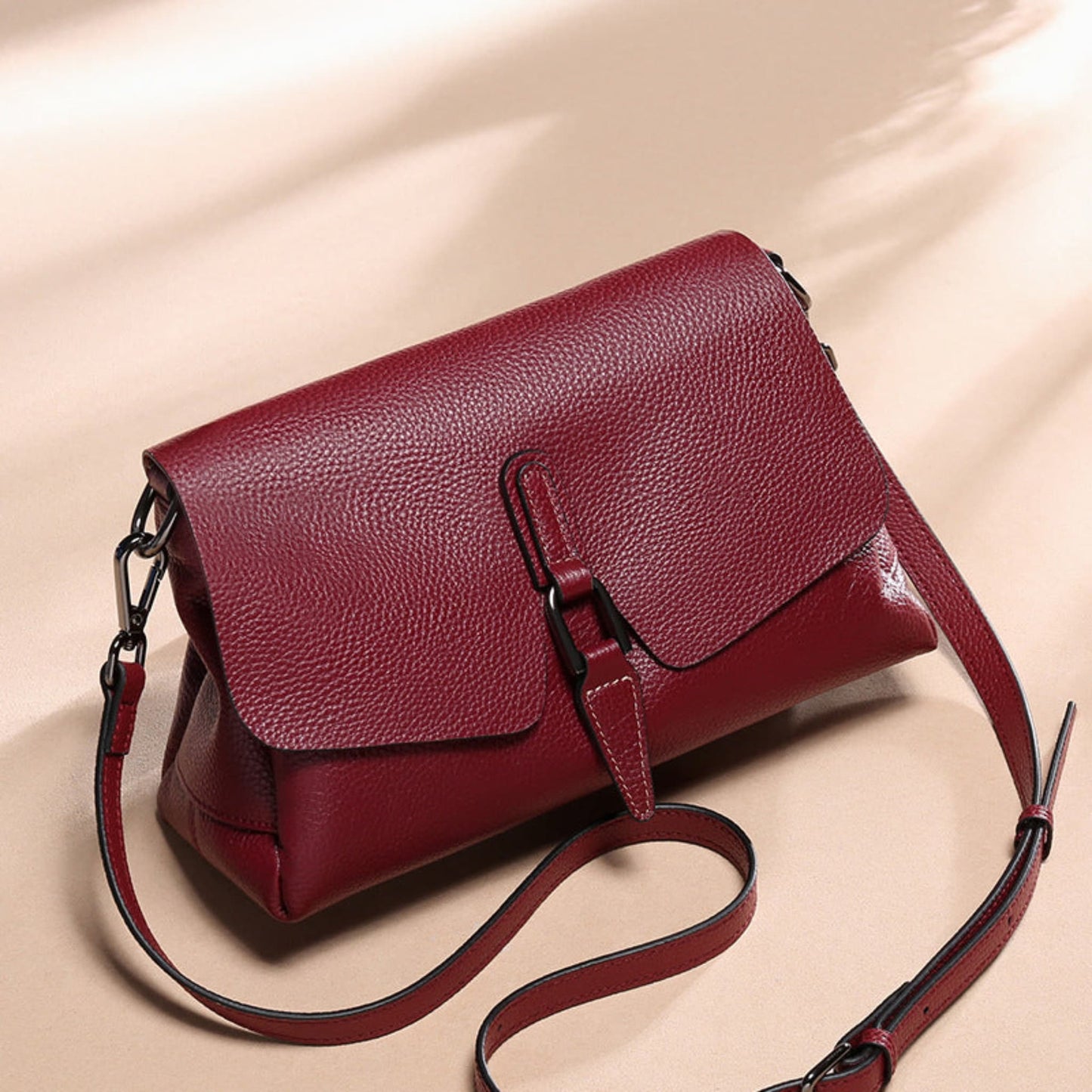 woMen's soft leather shoulder messenger bag in wine red on beige background showing adjustable strap position | Avenue