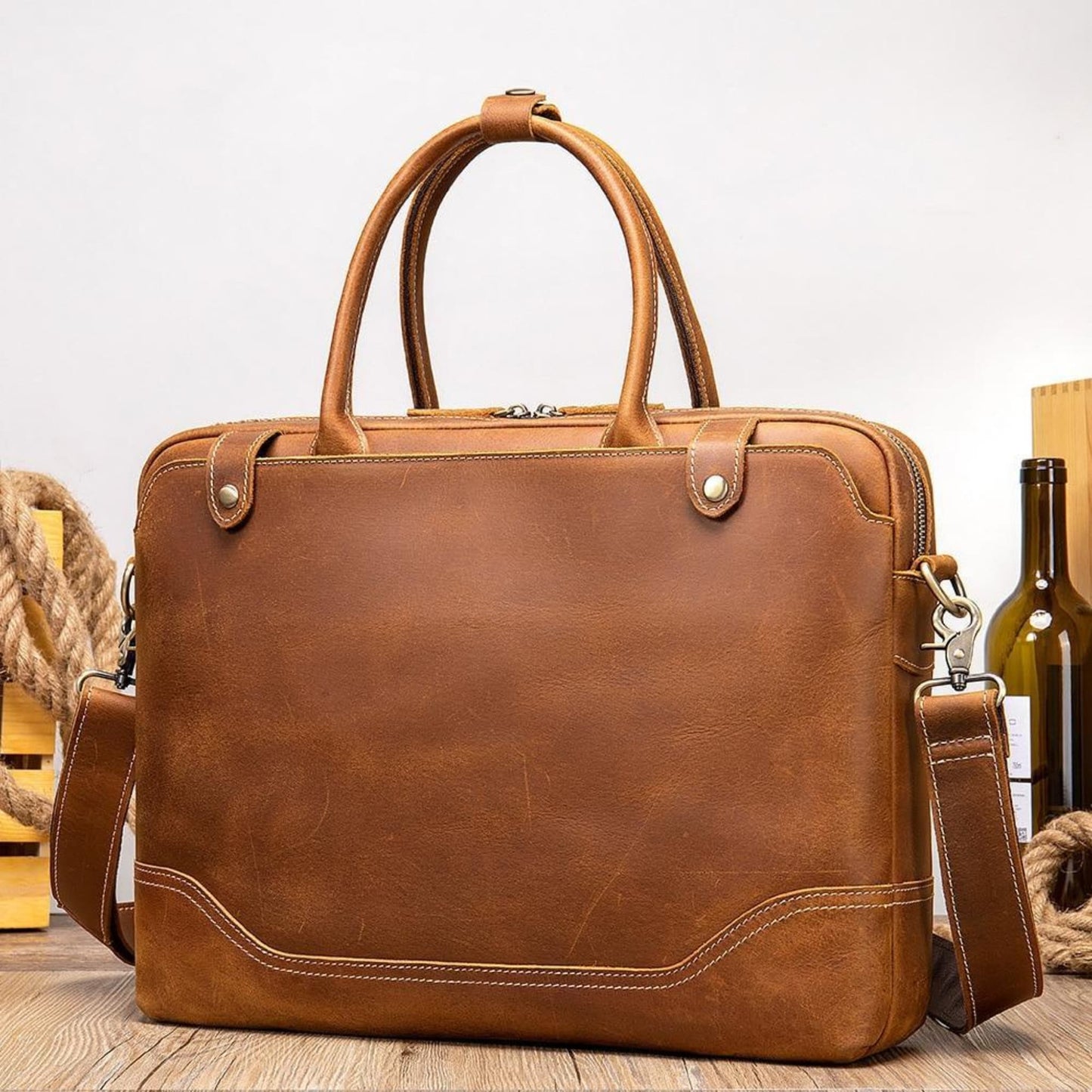 Avenue Crazy Horse Leather Men's Laptop Briefcase — coffee, front lifestyle view on wooden surface with rope and wine bottle, dual handles, brass zipper, shoulder strap, retro vintage style