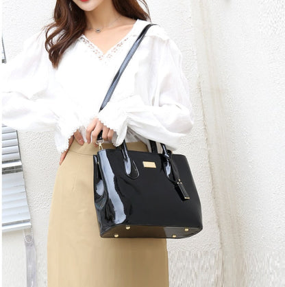 Woman wearing glossy PU leather tote bag in black as shoulder bag, styled with white blouse and beige skirt | Avenue