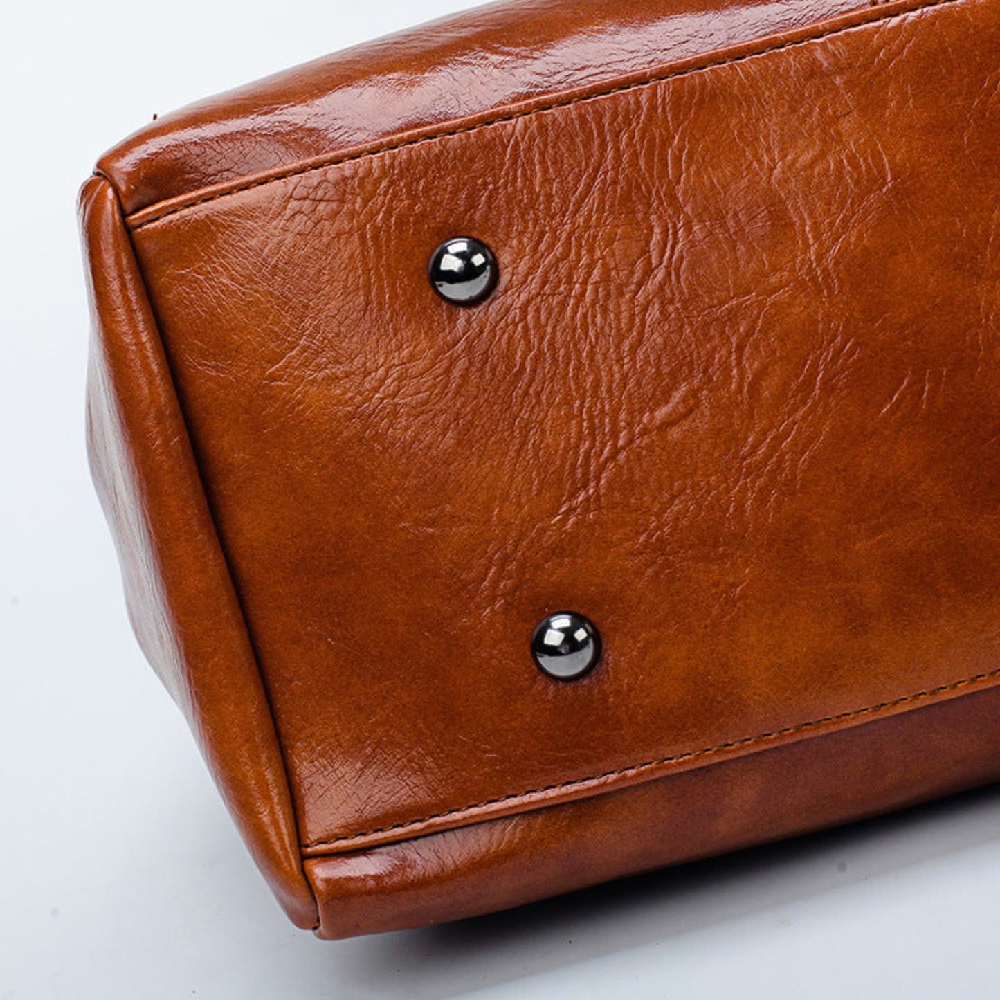 Women's vintage oil wax PU handbag in Brown displaying silver studs at the bottom close-up view onGrey background | Avenue