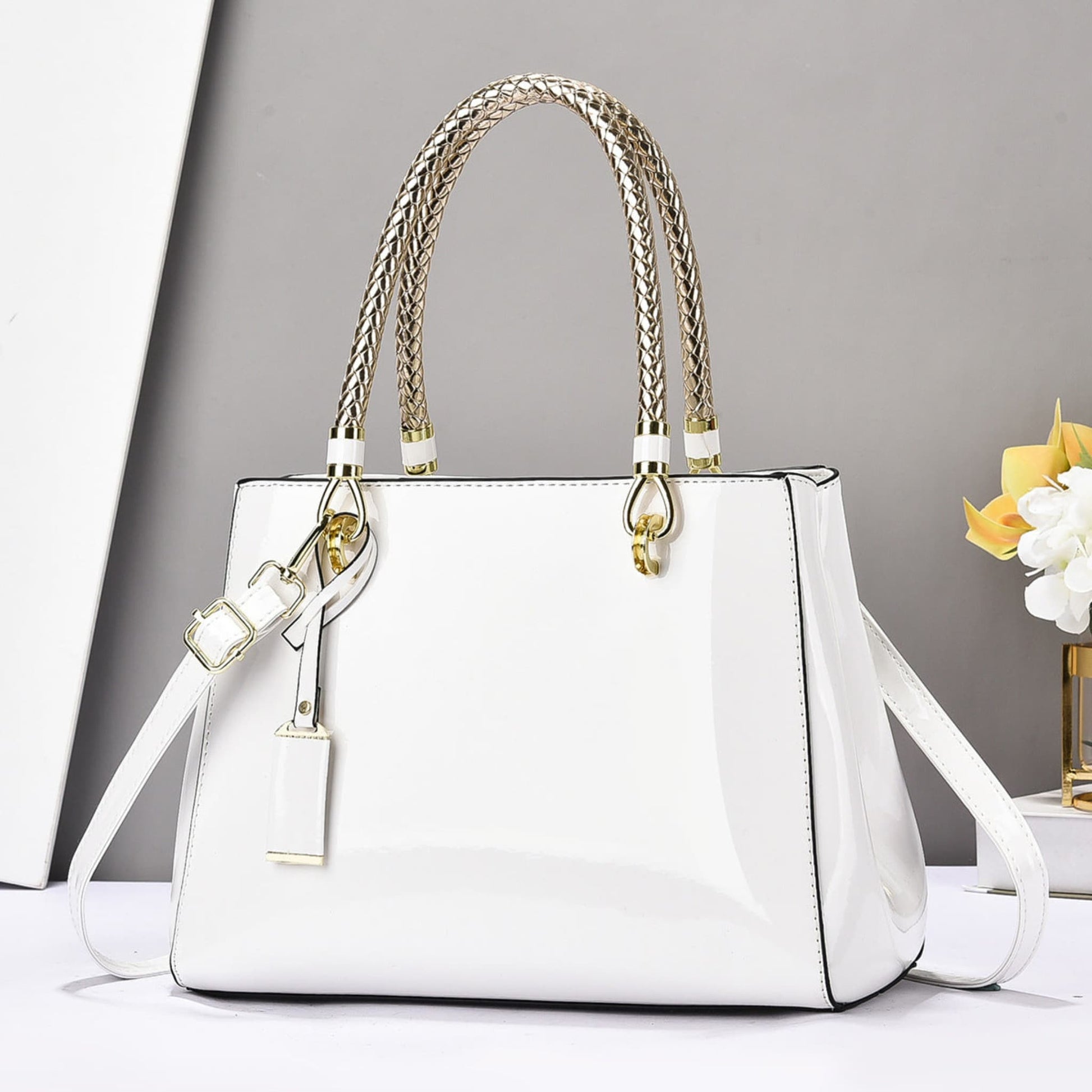 White glossy patent leather shoulder bag with gold accents on a white surface and grey background | Avenue