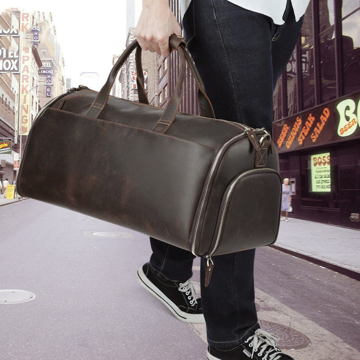 Men's Crazy Horse Leather Retro Duffle Bag – First Layer Cowhide Travel Bag in Coffee, lifestyle shot of man carrying bag by top handle on city street showing full size, side end zipper pocket and vintage retro aesthetic | Avenue