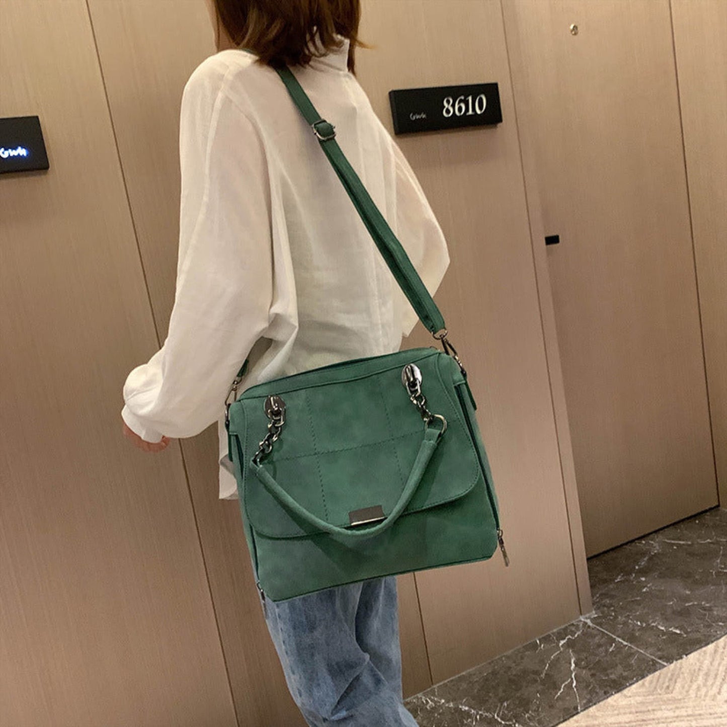 Woman wearing green matte PU leather large capacity Boston shoulder tote bag crossbody style with adjustable strap and silver chain hardware, styled with white top and blue jeans — Avenue
