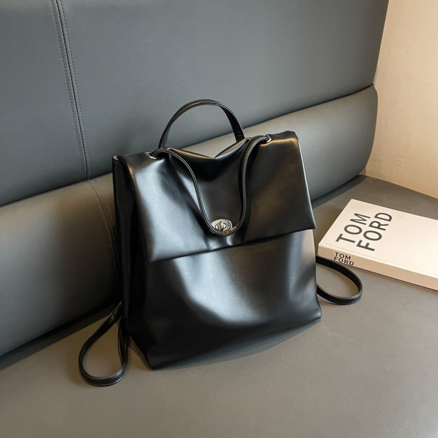 Women's Retro Flap Backpack in Black – Lifestyle Shot Styled with Tom Ford Book, Turn-Lock Closure and Top Handle | Avenue