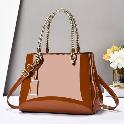 Brown glossy patent leather shoulder bag with gold accents on a white surface and grey background | Avenue