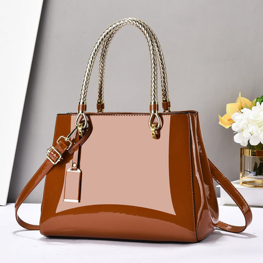 Brown glossy patent leather shoulder bag with gold accents on a white surface and grey background | Avenue