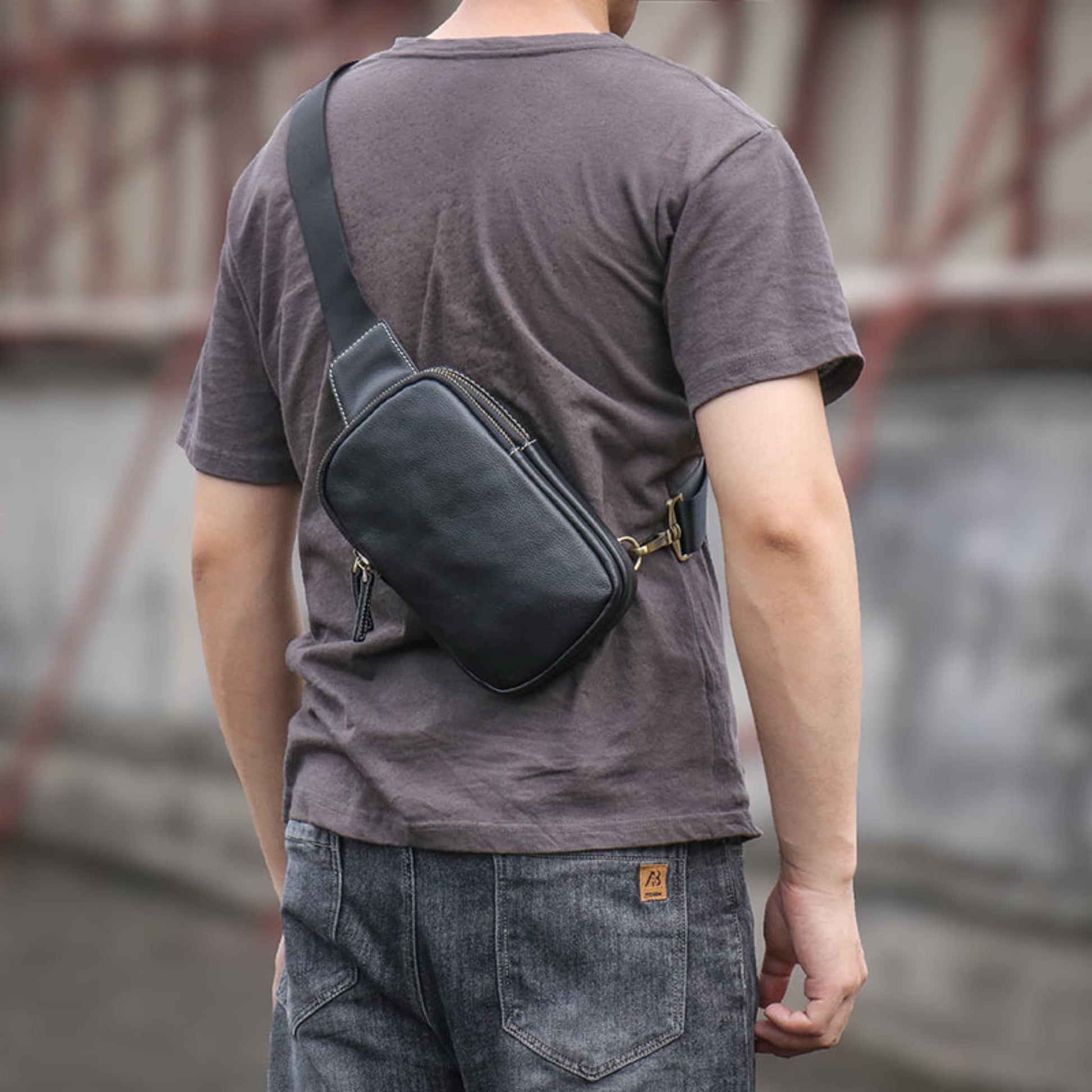 Rear view of man wearing Men's premium leather chest crossbody bag in black with gold zipper and adjustable strap — Avenue