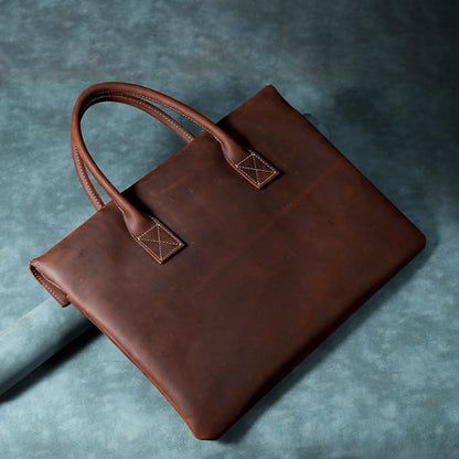 Avenue Vintage Crazy Horse Leather Briefcase – 15 Inch Laptop Bag for Men & Women, Brown crazy horse cowhide, top-down angled view showing natural leather texture, contrast stitching and dual top handles on dark background