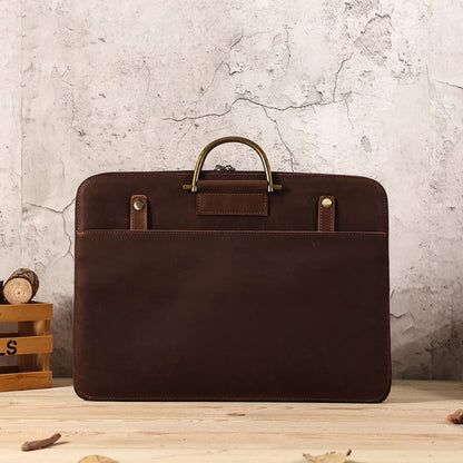 Avenue Crazy Horse Genuine Leather Briefcase for Men – Front view in 2121 Brown, featuring antique brass top handle, brass stud detailing, front slip pocket, and contrast stitching, styled on a wooden surface against a rustic stone wall background