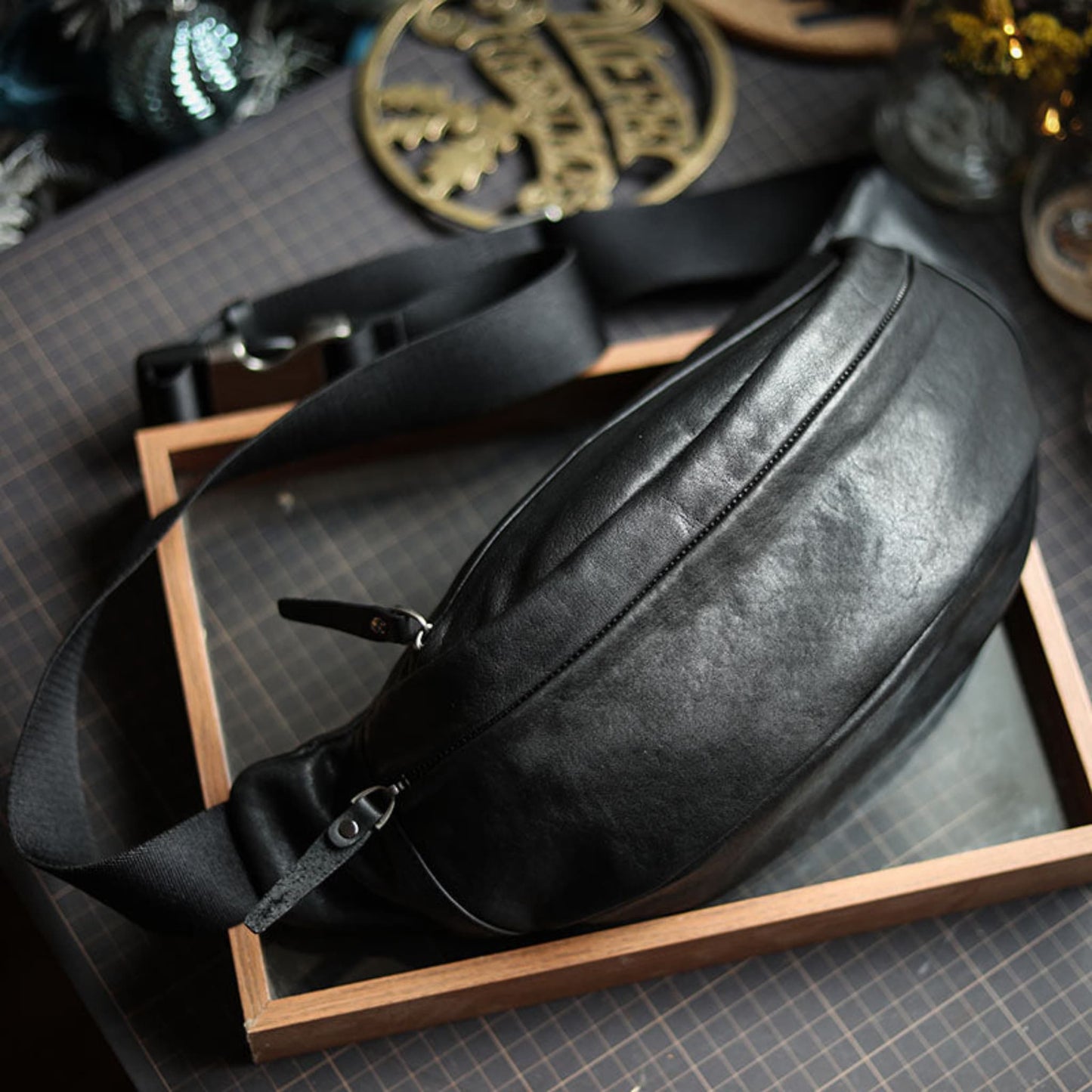 Men's black plant-tanned cow leather crossbody mobile phone bag with zipper closure and adjustable strap, displayed on wooden tray — Avenue