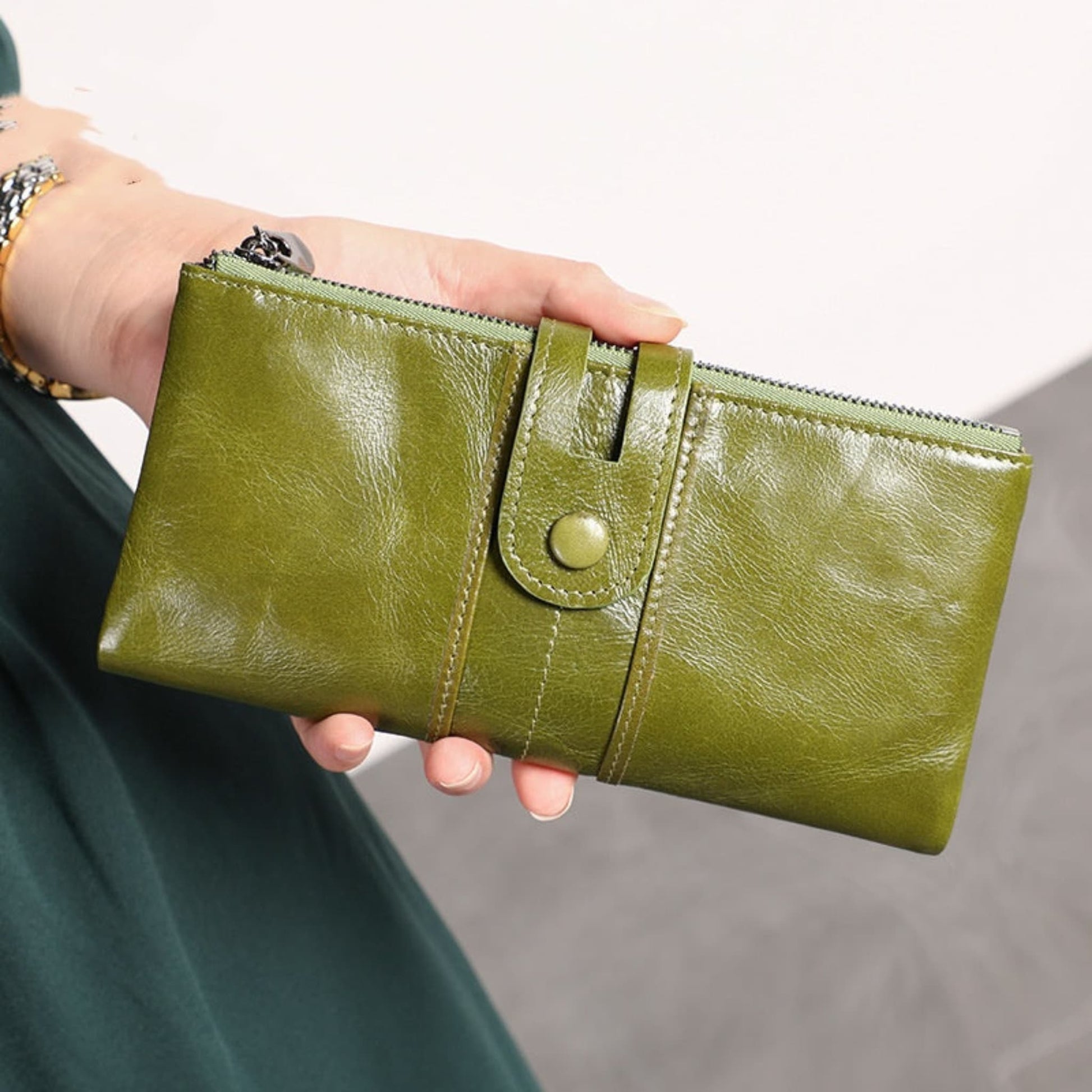 Women's RFID Long Leather Wallet first layer cowhide in Green – woman holding upright showing full front with strap closure and zipper | Avenue
