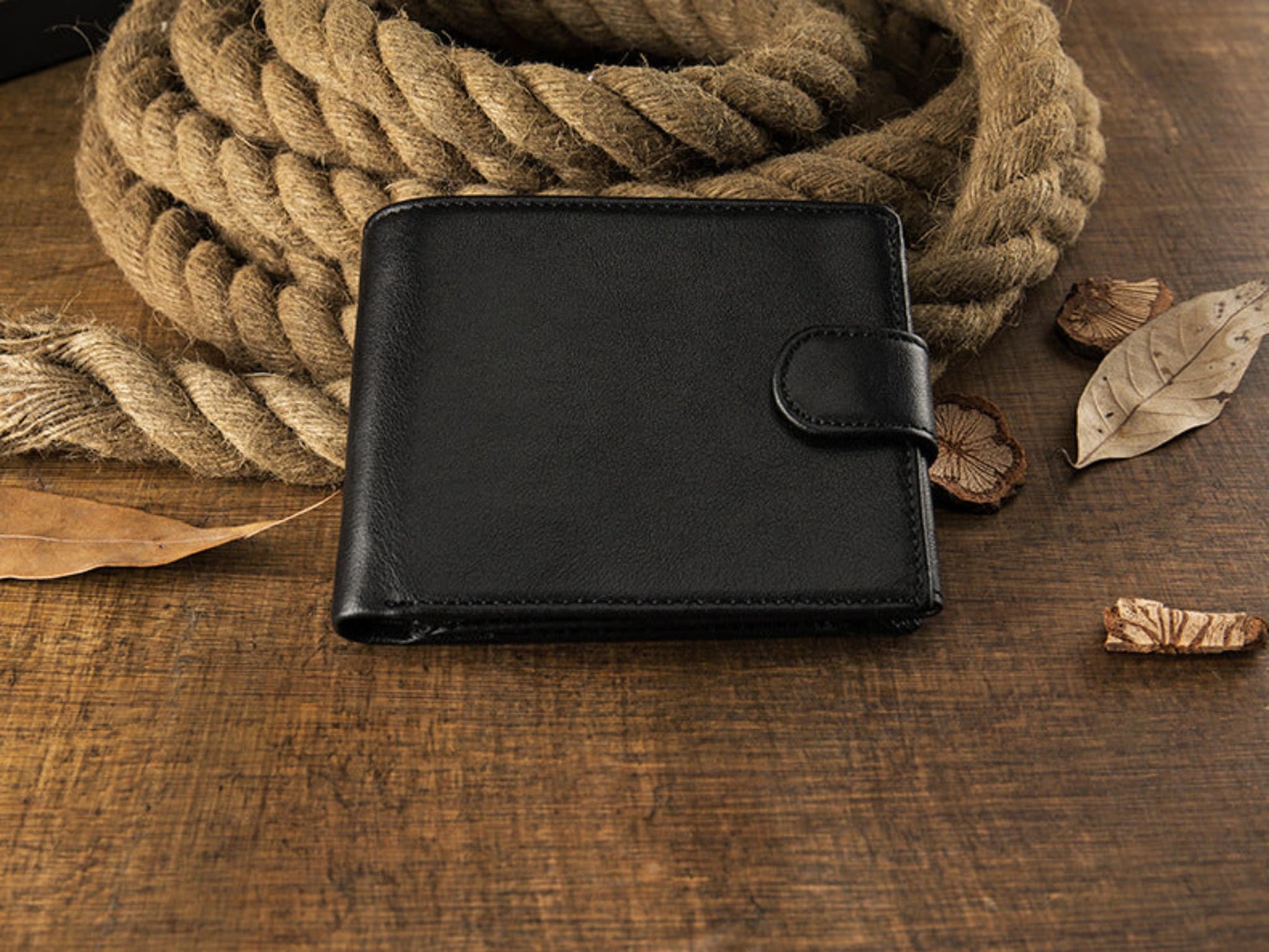 Avenue Men's Short Leather Wallet – Genuine Cowhide in Black, front view with snap closure, displayed on rustic rope and wooden surface