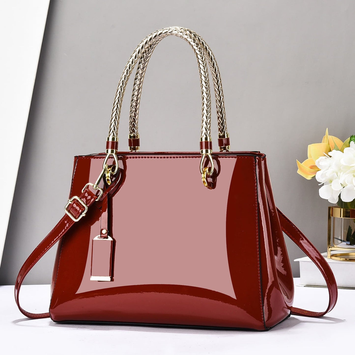 Red glossy patent leather shoulder bag with gold accents on a white surface and grey background | Avenue