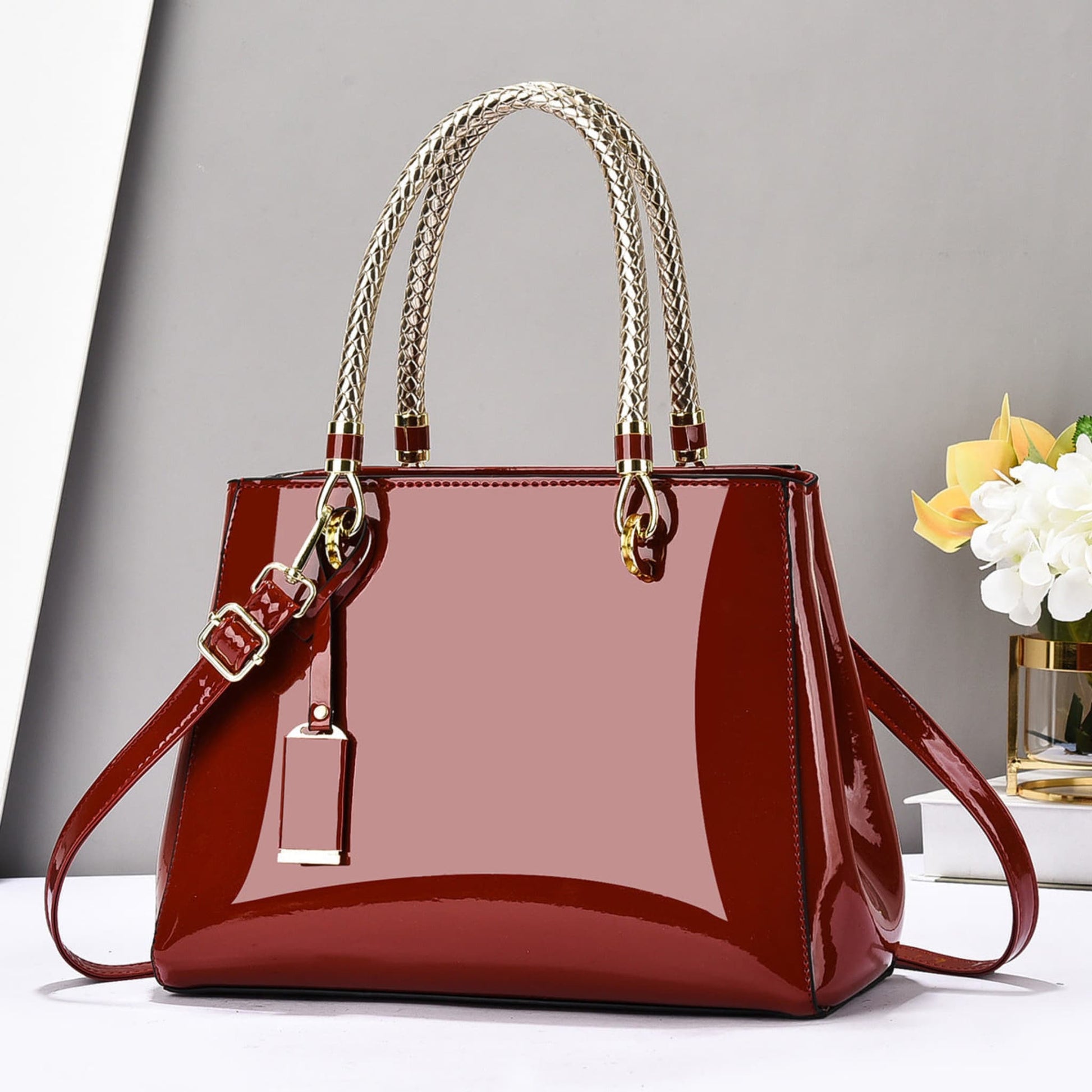 Red glossy patent leather shoulder bag with gold accents on a white surface and grey background | Avenue