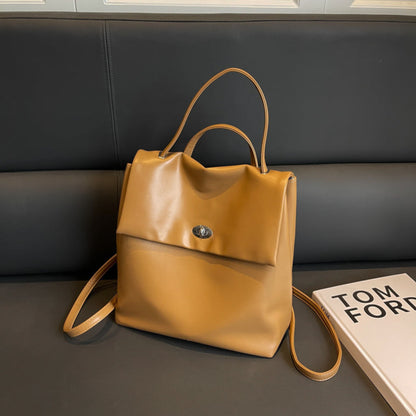 Women's Retro Flap Backpack in Brown – Lifestyle Shot on Sofa Styled with Tom Ford Book, Turn-Lock Closure and Dual Backpack Straps | Avenue