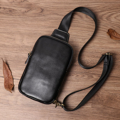 Men's premium leather chest crossbody bag in black with gold zipper and adjustable strap laid flat on wooden surface — Avenue