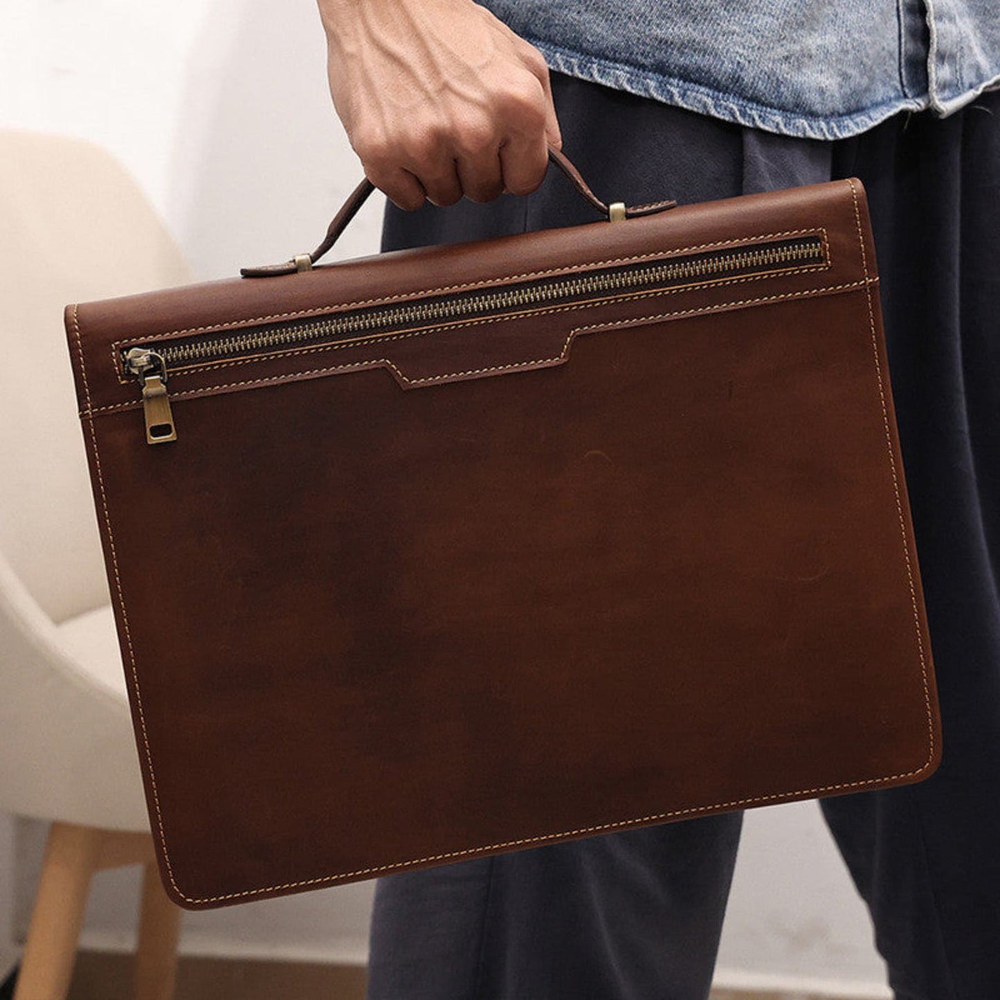 Avenue Men's Crazy Horse Leather Laptop Briefcase 13.3 Inch — Man Holding Briefcase by Top Handle Showing Back Zipper Pocket and Contrast Stitching in Coffee Brown