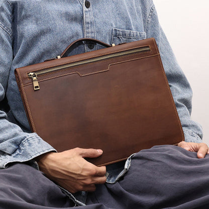 Avenue Men's Crazy Horse Leather Laptop Briefcase 13.3 Inch — Man Seated Holding Briefcase on Lap Showing Back Zipper Pocket, Top Handle and Gold Hardware in Coffee Brown