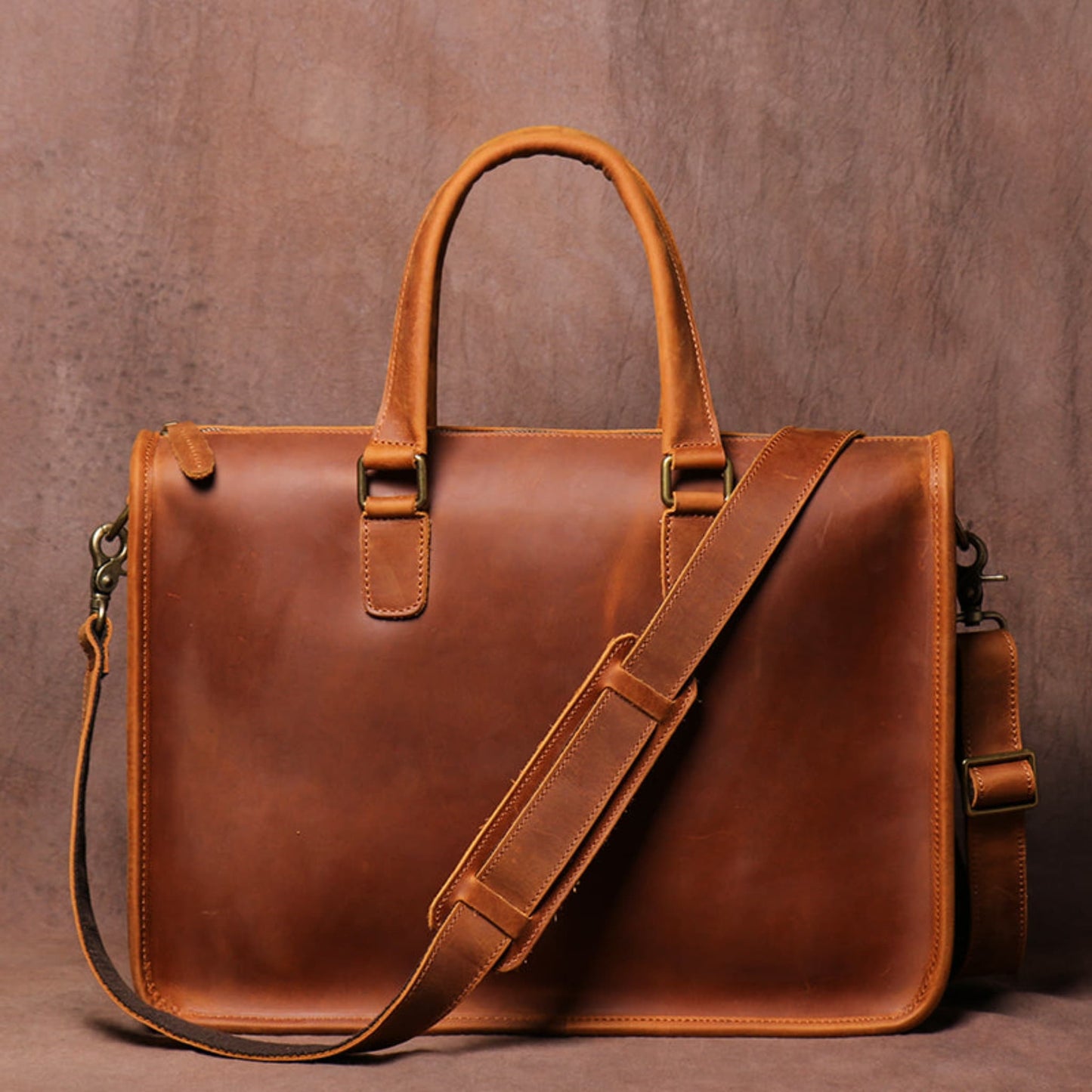 Men's Crazy Horse Leather Briefcase | Vintage Laptop Bag – Vintage Brown Front View with Top Handles, Antique Brass Hooks and Shoulder Strap on Vintage Brown Textured Background by Avenue