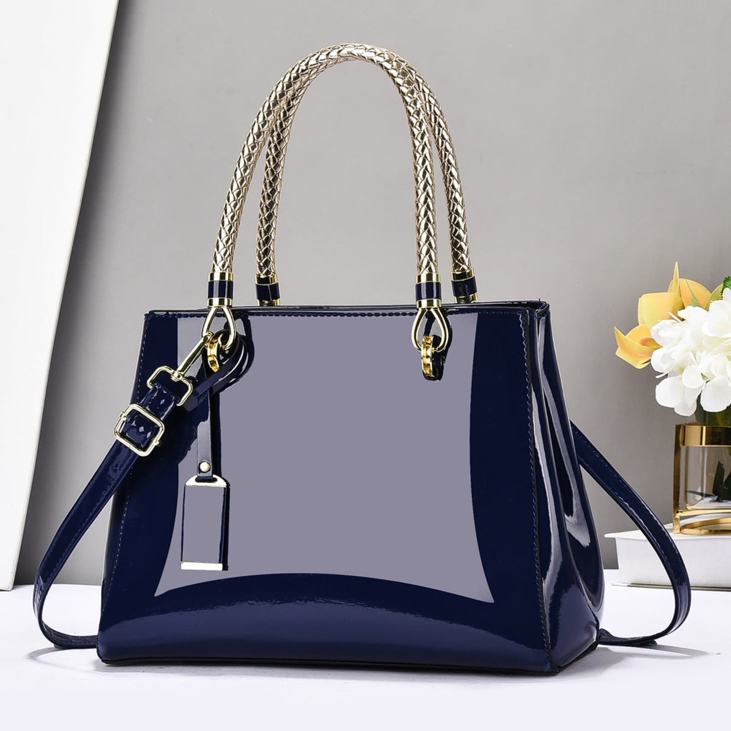Blue glossy patent leather shoulder bag with gold accents on a white surface and grey background | Avenue