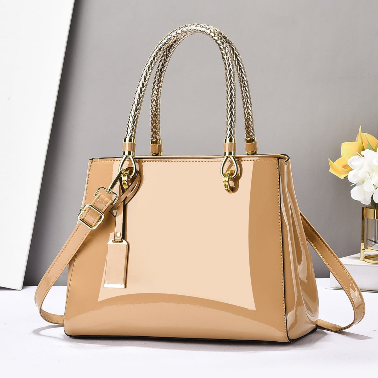 Khaki glossy patent leather shoulder bag with gold accents on a white surface and grey background | Avenue