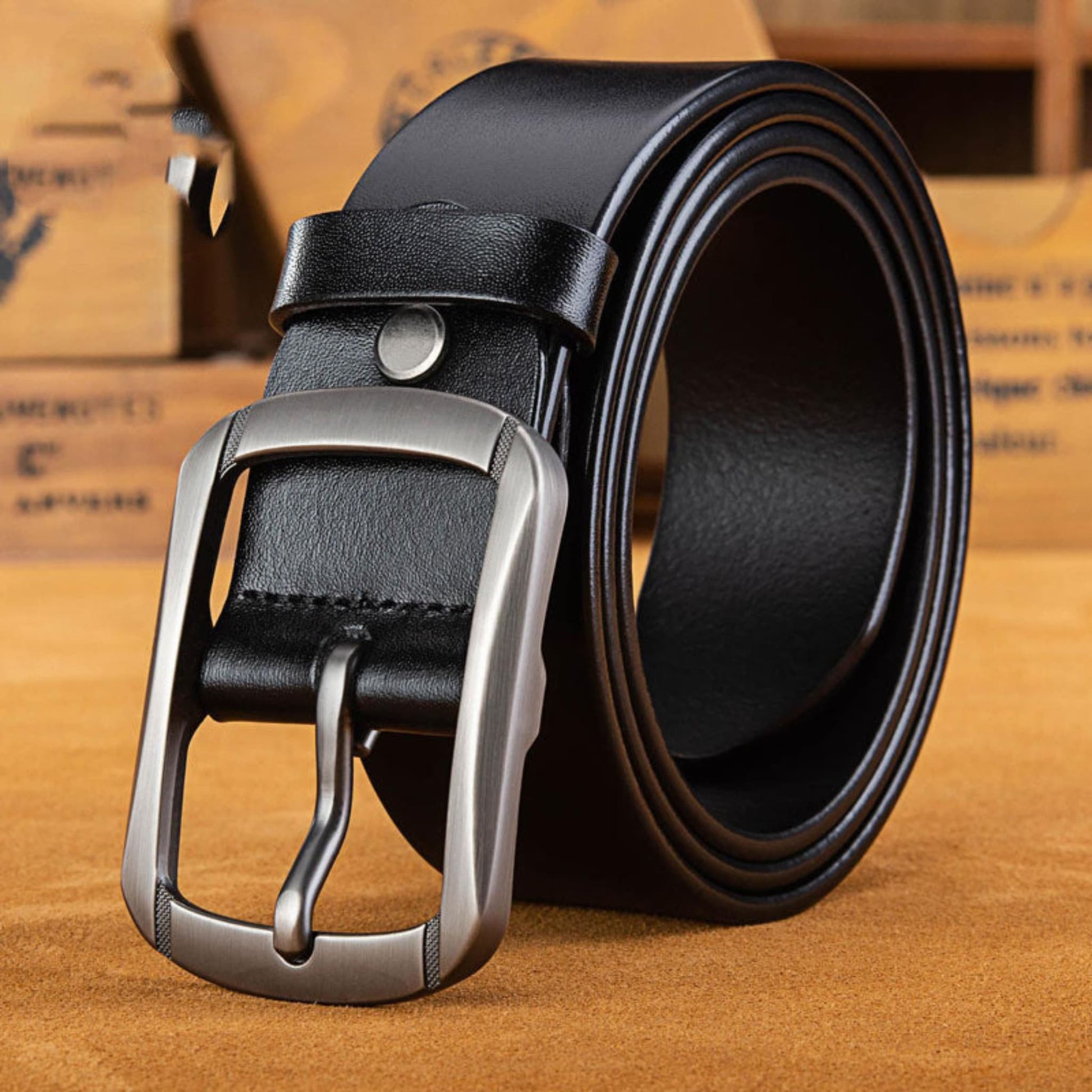 Men's full-grain cowhide leather belt in black with silver pin buckle, coiled and laying flat on tan leather surface | Avenue