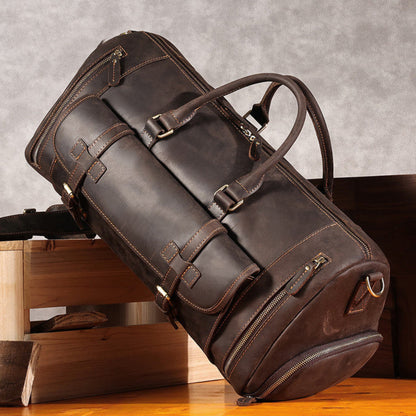 Avenue’s coffee Top-Grain Cowhide Leather Travel Duffle Bag with twin carry handles, displayed on wooden furniture against a textured grey background.