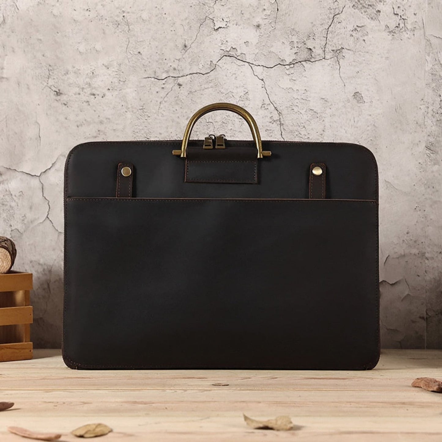 Avenue Crazy Horse Genuine Leather Briefcase for Men – Front view in 2121 Coffee, featuring antique brass top handle and clasp, brass stud detailing, front slip pocket, styled on a wooden surface against a rustic stone wall background
